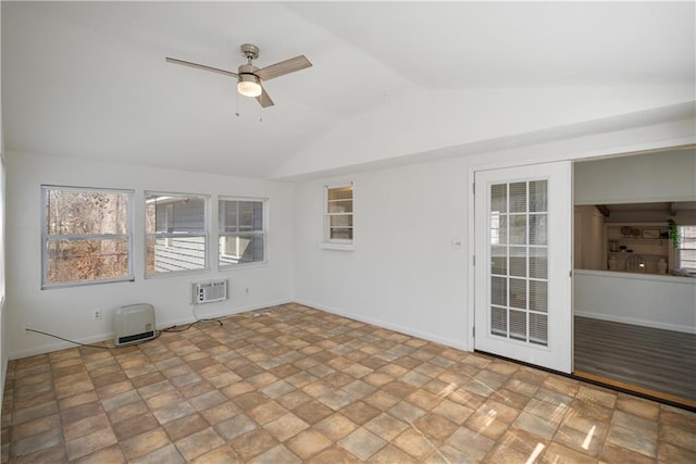 empty room with baseboards, a wall unit AC, ceiling fan, stone finish flooring, and vaulted ceiling