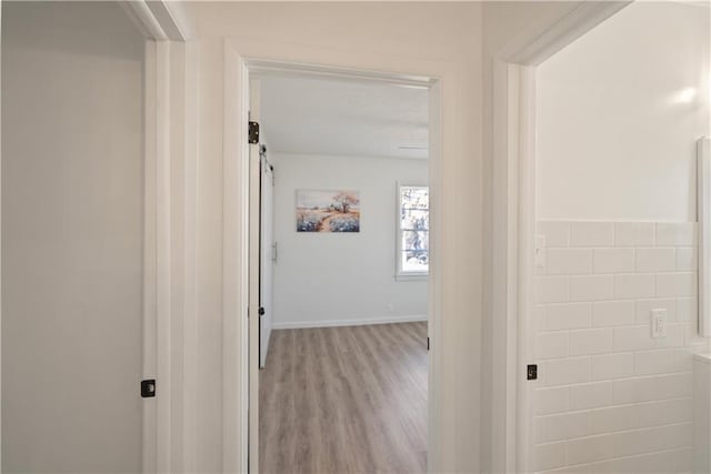 corridor with baseboards, light wood finished floors, and a barn door