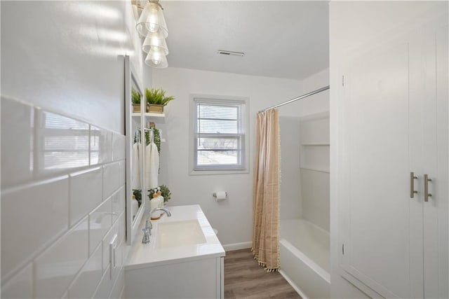 bathroom featuring wood finished floors, vanity, visible vents, baseboards, and shower / bath combo with shower curtain