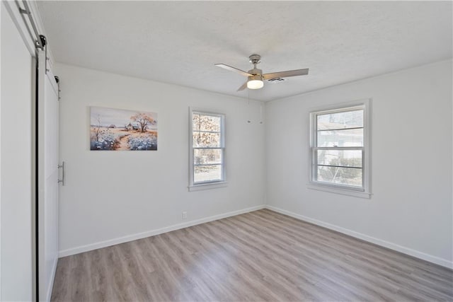 spare room with light wood finished floors, a barn door, baseboards, and a wealth of natural light