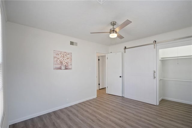 unfurnished bedroom with a closet, visible vents, a barn door, wood finished floors, and baseboards