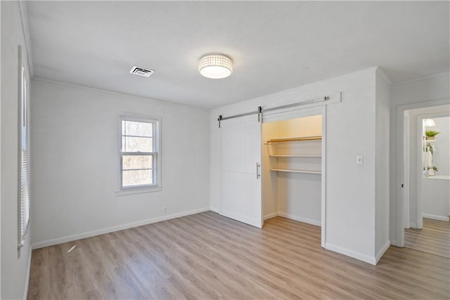 unfurnished bedroom featuring a barn door, a closet, light wood-type flooring, and baseboards