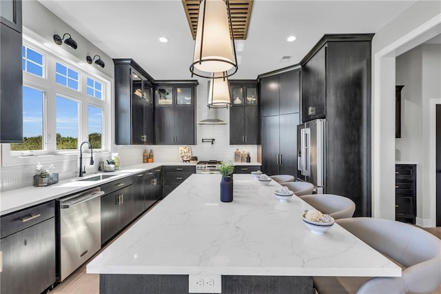 kitchen featuring light stone counters, wall chimney exhaust hood, hanging light fixtures, and a breakfast bar area