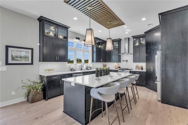 kitchen featuring wall chimney range hood, a kitchen island, glass insert cabinets, and light countertops