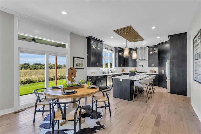 kitchen featuring light countertops, hanging light fixtures, glass insert cabinets, a kitchen island, and wall chimney exhaust hood