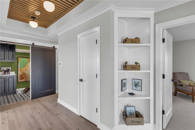 hall featuring a barn door, ornamental molding, a tray ceiling, light wood-style floors, and built in shelves