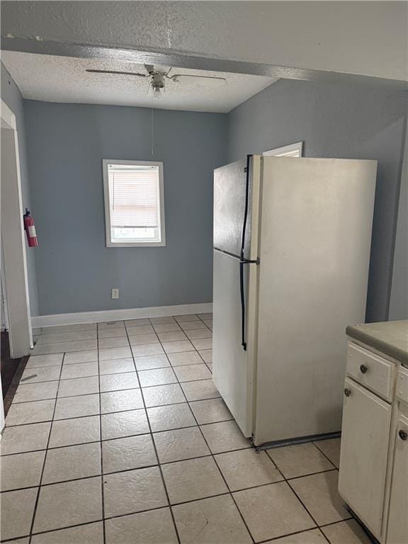 kitchen featuring light tile patterned floors, a ceiling fan, freestanding refrigerator, a textured ceiling, and white cabinetry