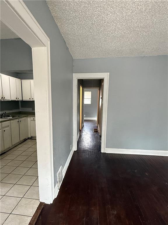 hallway with a textured ceiling, visible vents, light wood-style flooring, and baseboards