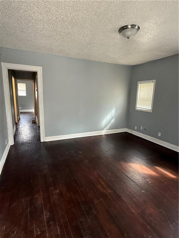 spare room featuring a healthy amount of sunlight, baseboards, and dark wood finished floors