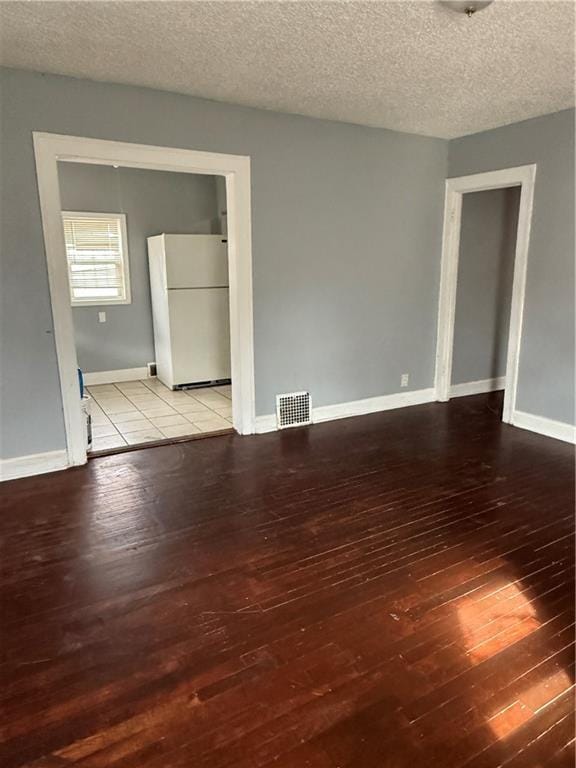 spare room featuring visible vents, a textured ceiling, baseboards, and hardwood / wood-style flooring