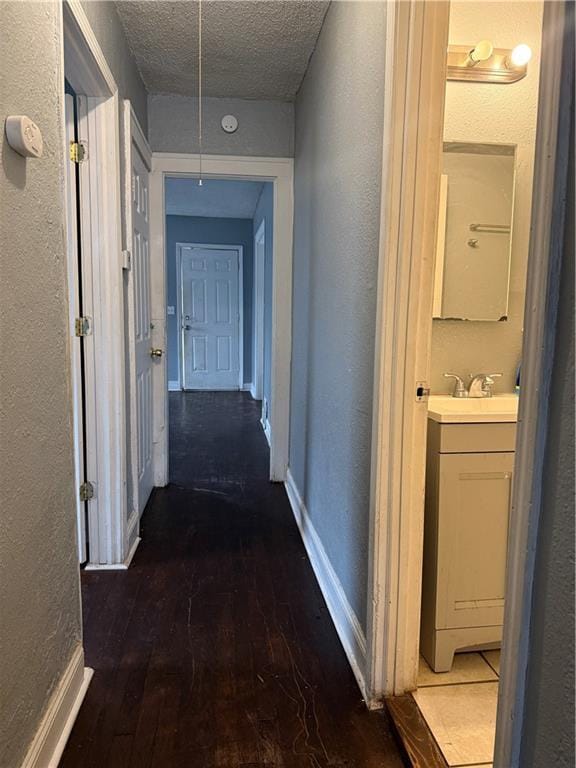 hall with a textured ceiling, a sink, baseboards, dark wood-style floors, and attic access