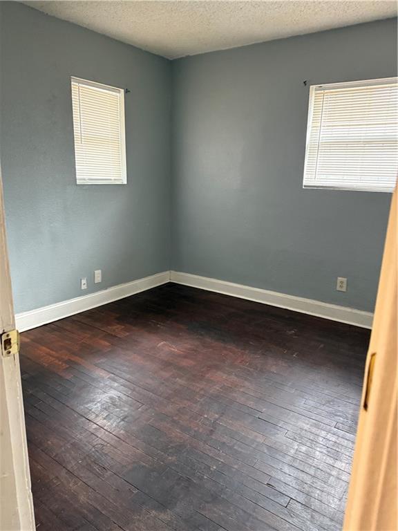 spare room with a textured ceiling, hardwood / wood-style flooring, and baseboards