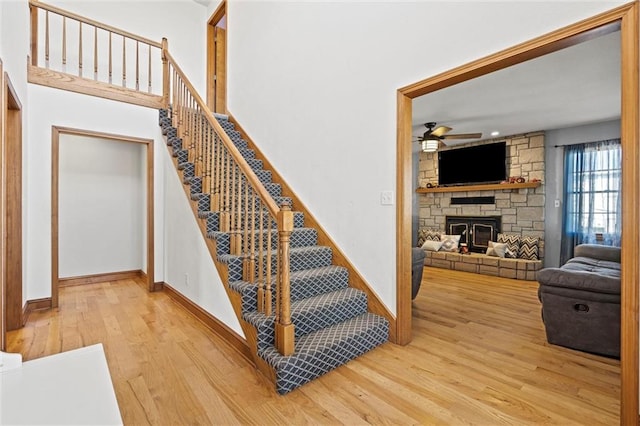 stairs featuring a fireplace, wood finished floors, baseboards, and ceiling fan