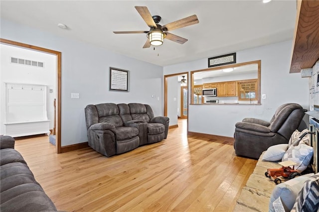 living room featuring light wood-style flooring, a ceiling fan, visible vents, and baseboards