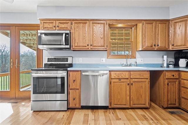 kitchen featuring light wood finished floors, a sink, stainless steel appliances, brown cabinetry, and light countertops