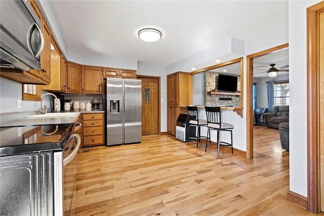 kitchen featuring light wood finished floors, light countertops, brown cabinets, stainless steel appliances, and a ceiling fan