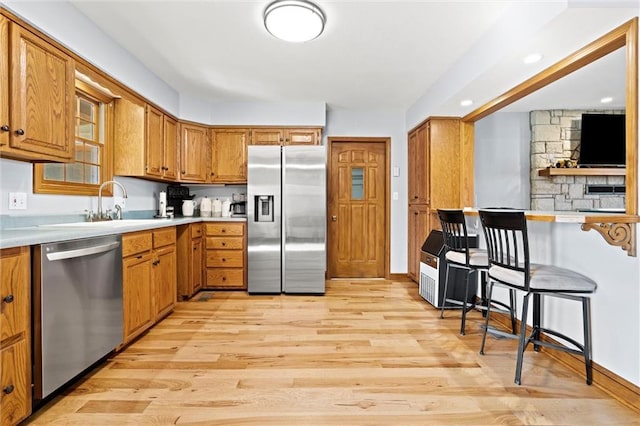 kitchen with stainless steel appliances, light wood-style flooring, brown cabinetry, and light countertops