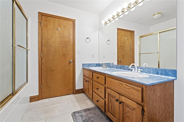 full bath featuring a sink, a textured ceiling, double vanity, and tile patterned floors