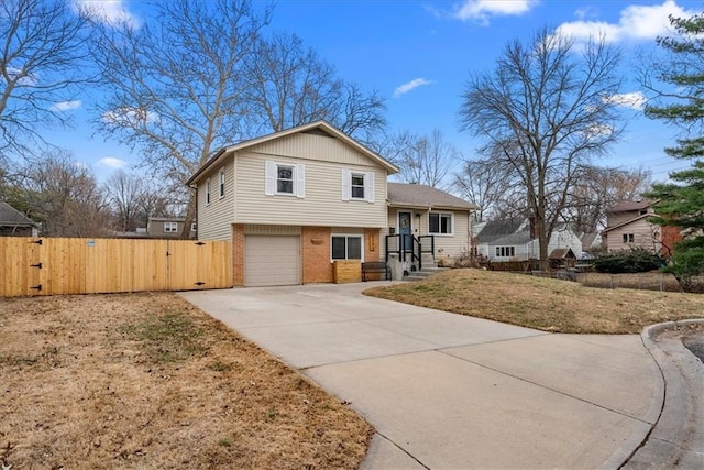 split level home with a gate, fence, concrete driveway, a garage, and brick siding