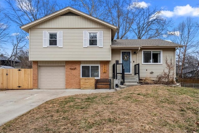 tri-level home with brick siding, an attached garage, fence, and a gate