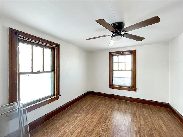 empty room with wood finished floors, a ceiling fan, and baseboards