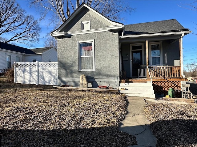 view of front of home featuring a shingled roof, covered porch, fence, and stucco siding