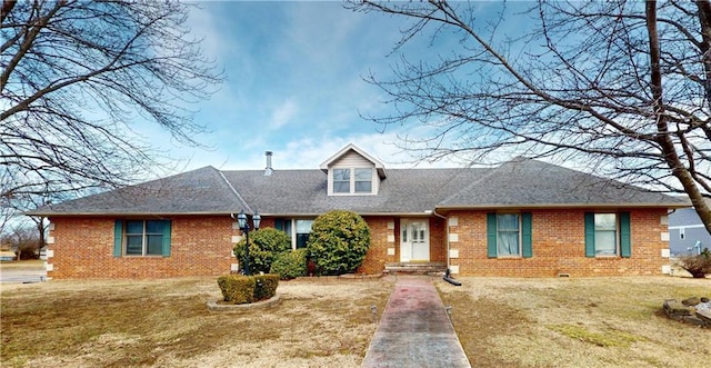 cape cod-style house with a shingled roof, a front yard, and brick siding