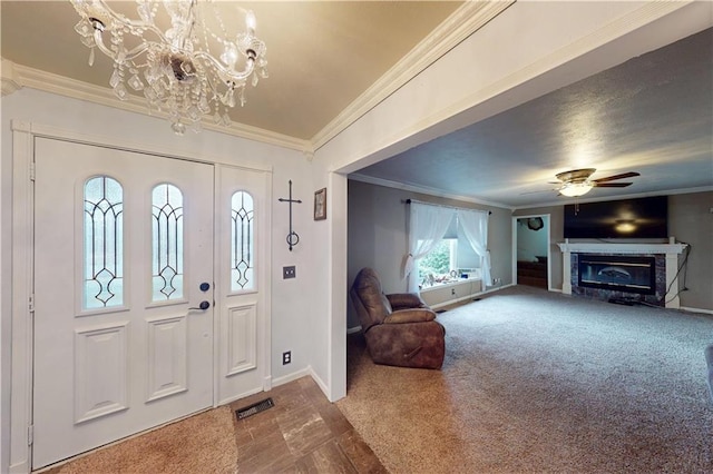 carpeted foyer featuring ceiling fan with notable chandelier, visible vents, baseboards, ornamental molding, and a glass covered fireplace