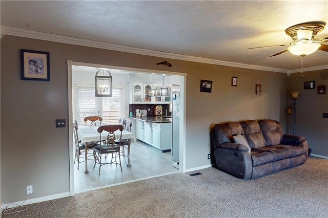 living room with a ceiling fan, baseboards, crown molding, and light colored carpet