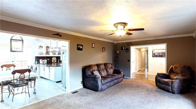 living room with ceiling fan, carpet floors, baseboards, and crown molding