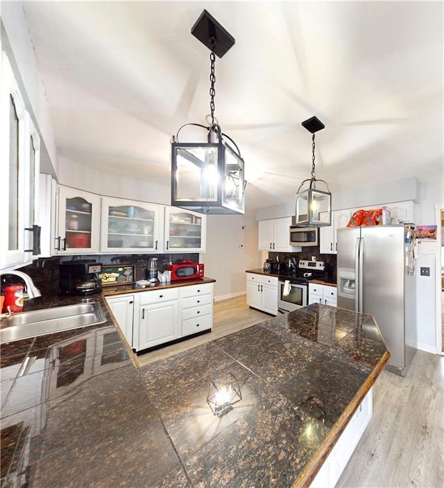 kitchen featuring tasteful backsplash, appliances with stainless steel finishes, glass insert cabinets, a peninsula, and a sink