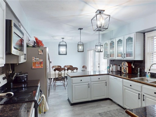 kitchen featuring stainless steel appliances, tasteful backsplash, white cabinetry, a sink, and a peninsula