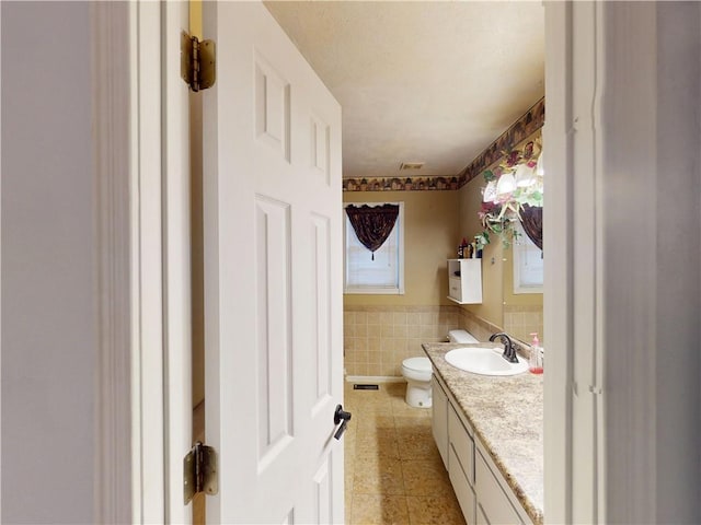 half bathroom featuring tile patterned flooring, toilet, vanity, tile walls, and wainscoting