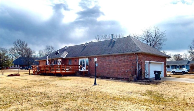 view of home's exterior featuring brick siding, a lawn, a deck, a garage, and driveway