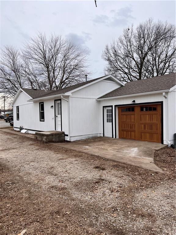 view of front facade featuring dirt driveway, roof with shingles, and an attached garage