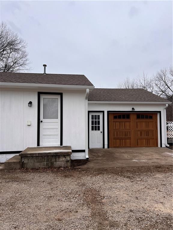 exterior space with roof with shingles, an attached garage, and dirt driveway