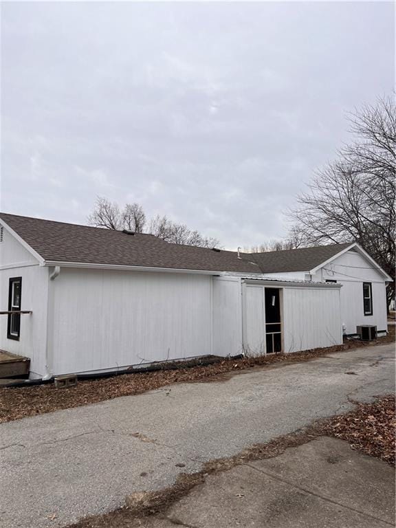 view of side of property featuring cooling unit and roof with shingles