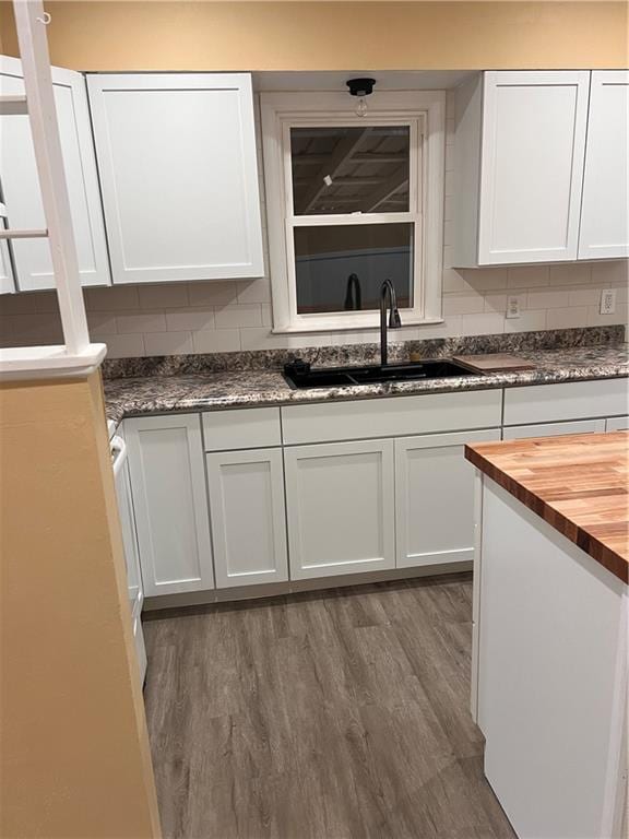 kitchen with dark wood-style floors, butcher block countertops, a sink, white cabinetry, and backsplash