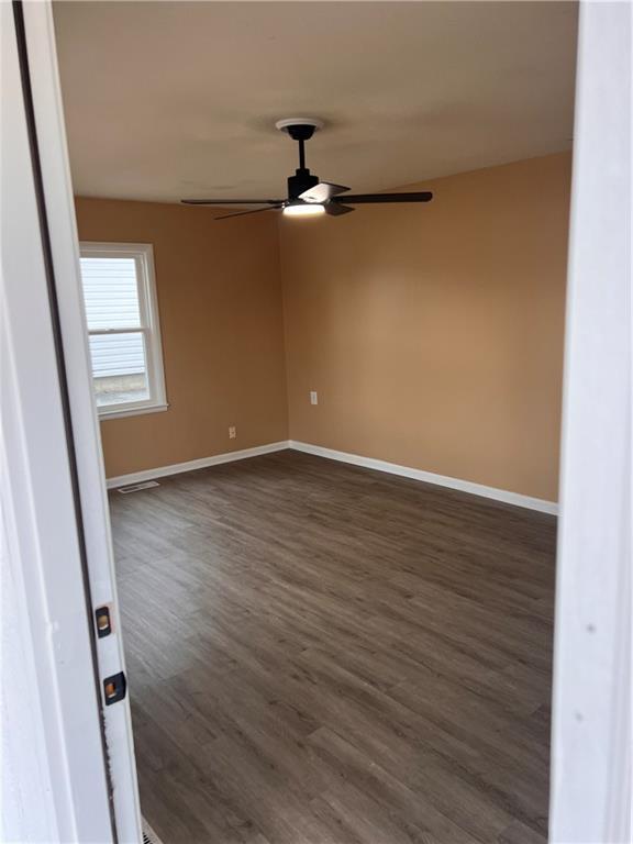 unfurnished room with ceiling fan, dark wood-type flooring, visible vents, and baseboards