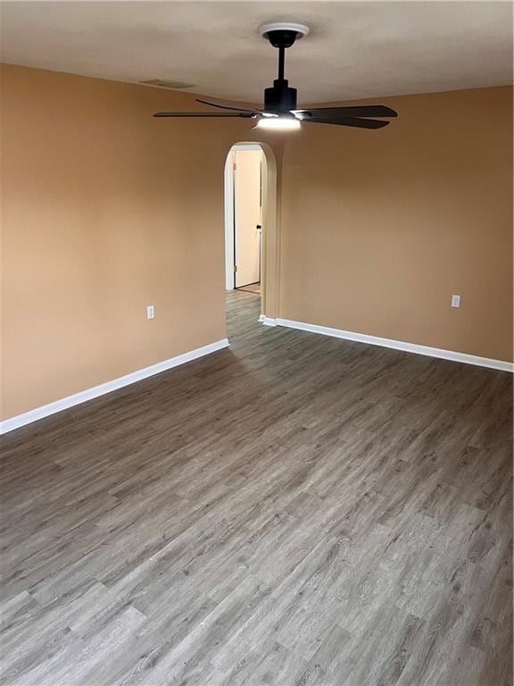 empty room with arched walkways, ceiling fan, wood finished floors, and baseboards