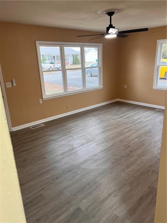 empty room featuring dark wood-style floors, plenty of natural light, visible vents, and baseboards