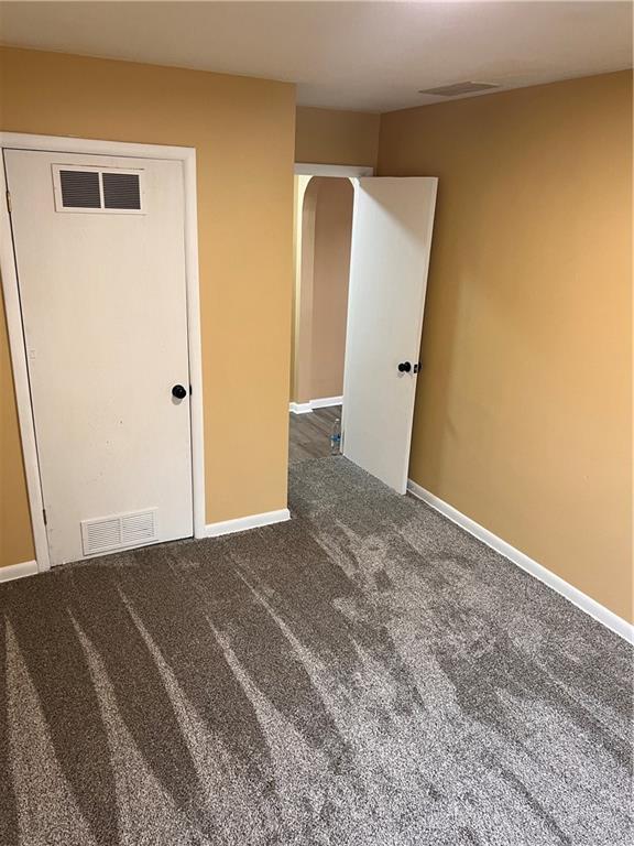 empty room with dark carpet, visible vents, and baseboards