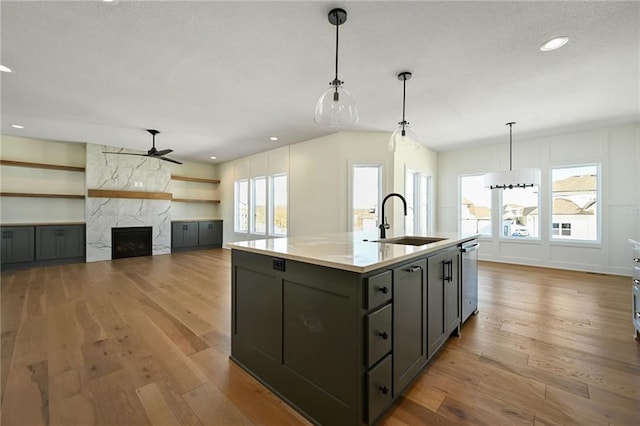 kitchen with a high end fireplace, open floor plan, a kitchen island with sink, a sink, and light wood-type flooring