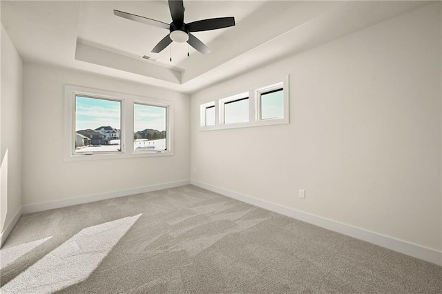 spare room featuring visible vents, a raised ceiling, light colored carpet, and baseboards