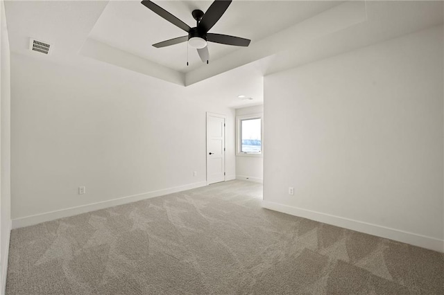 empty room featuring a tray ceiling, visible vents, carpet flooring, ceiling fan, and baseboards