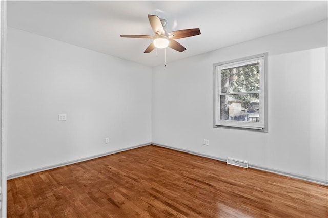 spare room with a ceiling fan, visible vents, baseboards, and wood finished floors