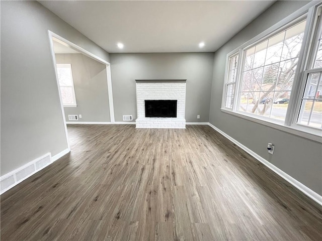 unfurnished living room featuring dark wood-style floors, baseboards, a brick fireplace, and visible vents