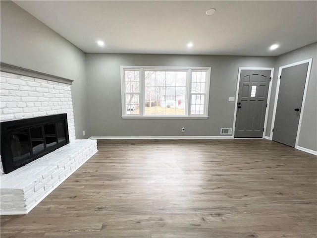 unfurnished living room with recessed lighting, visible vents, baseboards, a brick fireplace, and dark wood-style floors