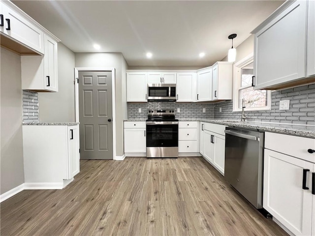 kitchen with hanging light fixtures, light stone counters, stainless steel appliances, and white cabinets