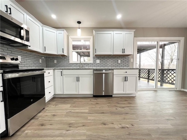 kitchen with hanging light fixtures, appliances with stainless steel finishes, white cabinets, and a sink